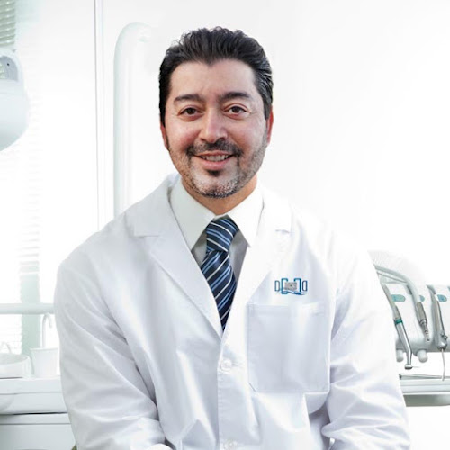 Portrait of happy male dentist wearing lab coat while sitting in clinic